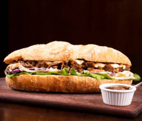 large shredded beef brisket sandwich with barbecue sauce on wooden board viewed from the front